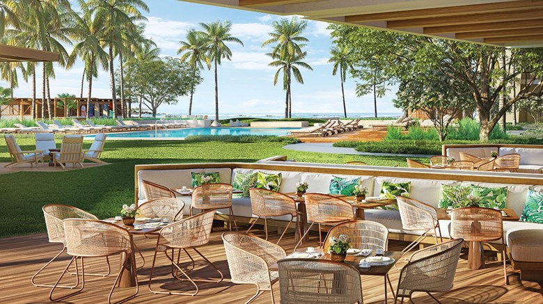 terrace dining patio with modern, wicker chairs and round tables. Views of the ocean with palm trees and other resort amenities in the periphery.