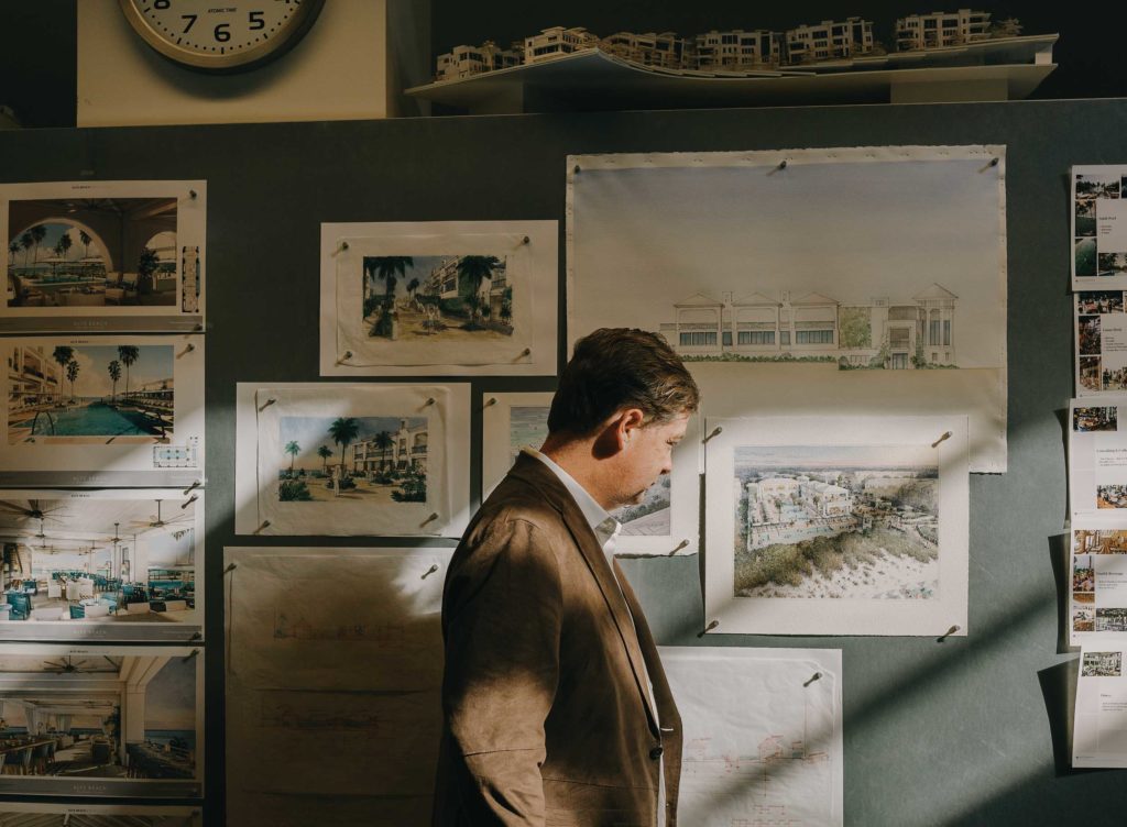 man looks at architectural watercolor renderings pinned up to a studio wall