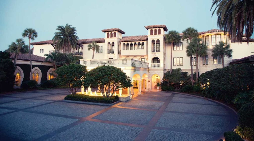 large resort hotel with addison mizner inspired architecture set amongst lush greenery and palm trees