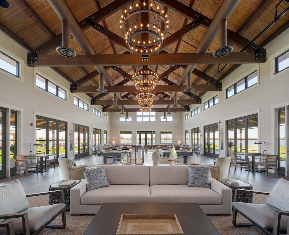 clubhouse ceiling with high ceilings and exposed beams. rustic contemporary chandeliers hang from the exposed beams throughout the center, a series of transitional club chairs and sofas are curated throughout the space to give the clubroom an open air feeling