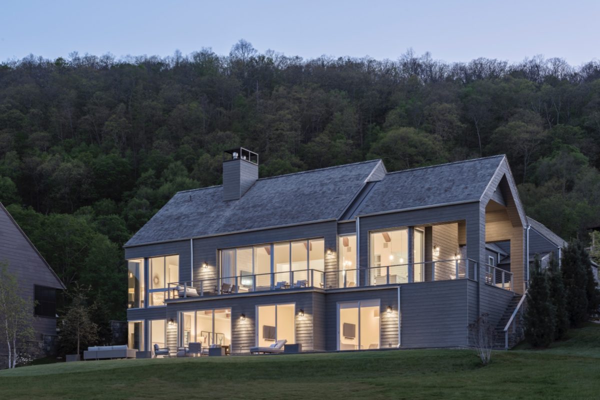 model home rendering in a modern farmhouse style with large windows lit up in a nightime setting of greenery surrounding in the hudson valley