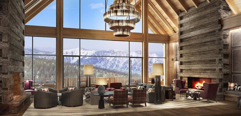 interior view of a large log cabin inspired hotel, large, floor to ceiling glass windows look out onto the rocky mountains where snow caps the landscape. Comfy club chairs and large, modern chandeliers adorn the living room space