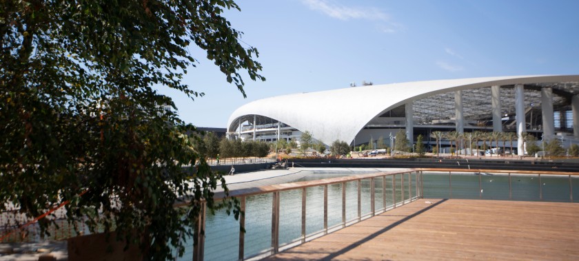 exterior image of the modern sofi football stadium. large modern white structure sits on a small lake with evergreen plantings surrounding