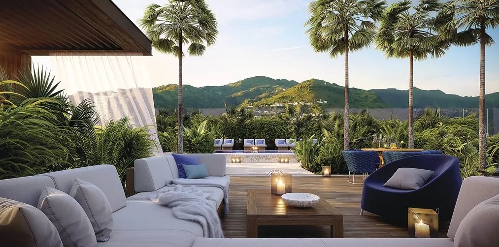 large palm trees flank a rooftop common space adorned with plush sectionals and overstuffed, modern lounge chairs. Views of rolling hills and volcano peak sit in the background