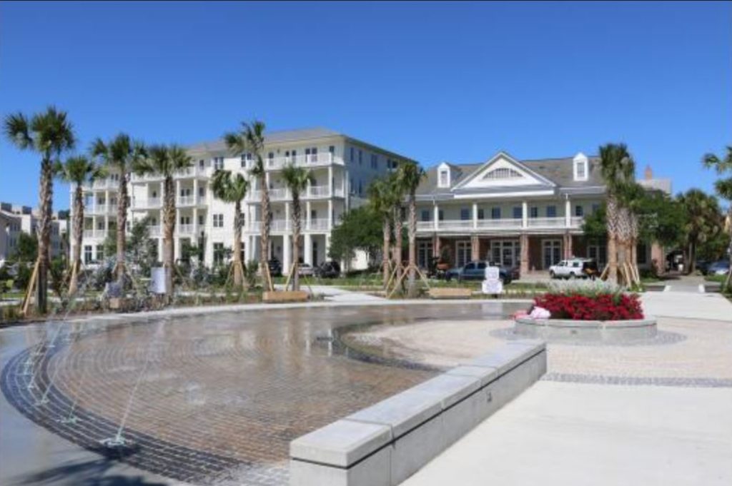 a water fountain with multifamily, white residential buildings in the background and palm trees
