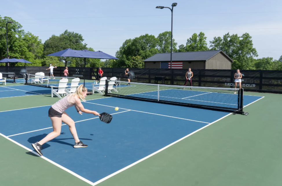 blue and green pickle ball court with two woman playing on either side of the net dressed in gym clothes