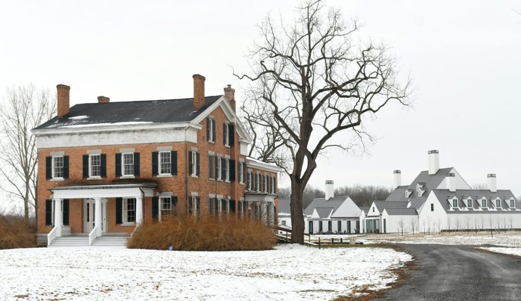 rural, snowy setting with a historic brick building and a white barn like structure in the background