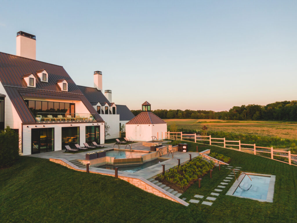 white barn house inspired building with a pool and plantings in the foreground